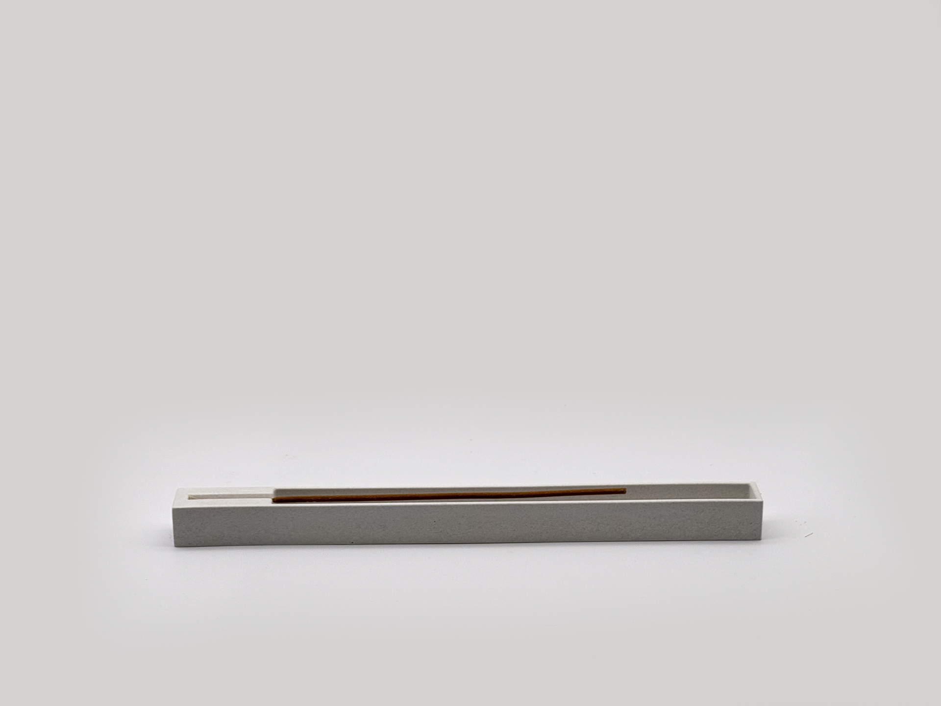 Single incense stick resting inside the concrete channel